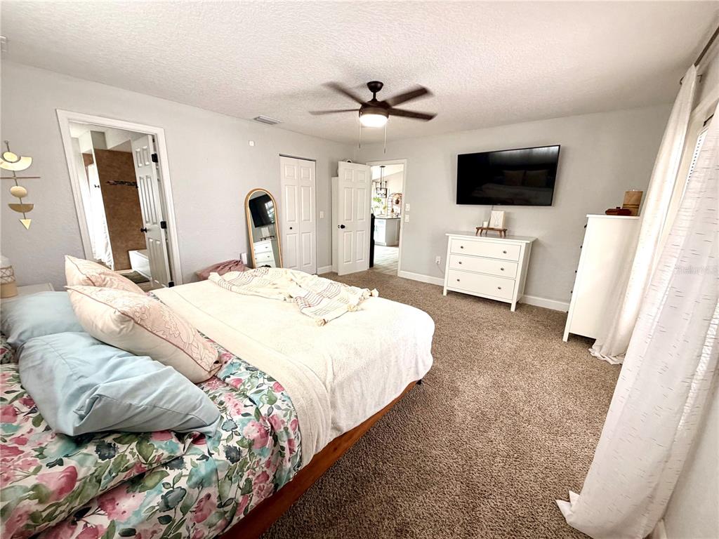 A bedroom features a bed with floral bedding, a wall-mounted television, and a white dresser — 11450 LINDEN DRIVE, SPRING HILL, FL