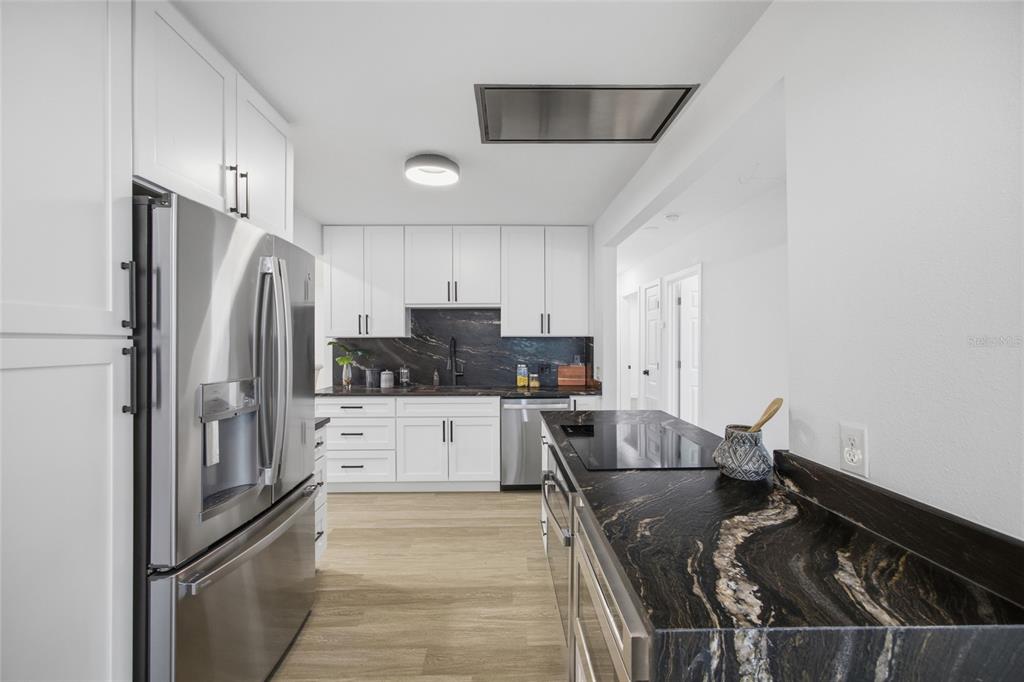 A modern kitchen features white cabinetry, stainless steel appliances, and dark stone countertops — 5207 W CLEVELAND STREET, TAMPA, FL