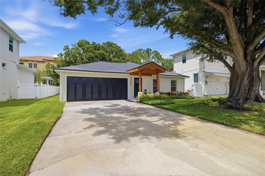 A single-story house with a white brick exterior, a dark garage door, and a wooden porch — 5207 W CLEVELAND STREET, TAMPA, FL