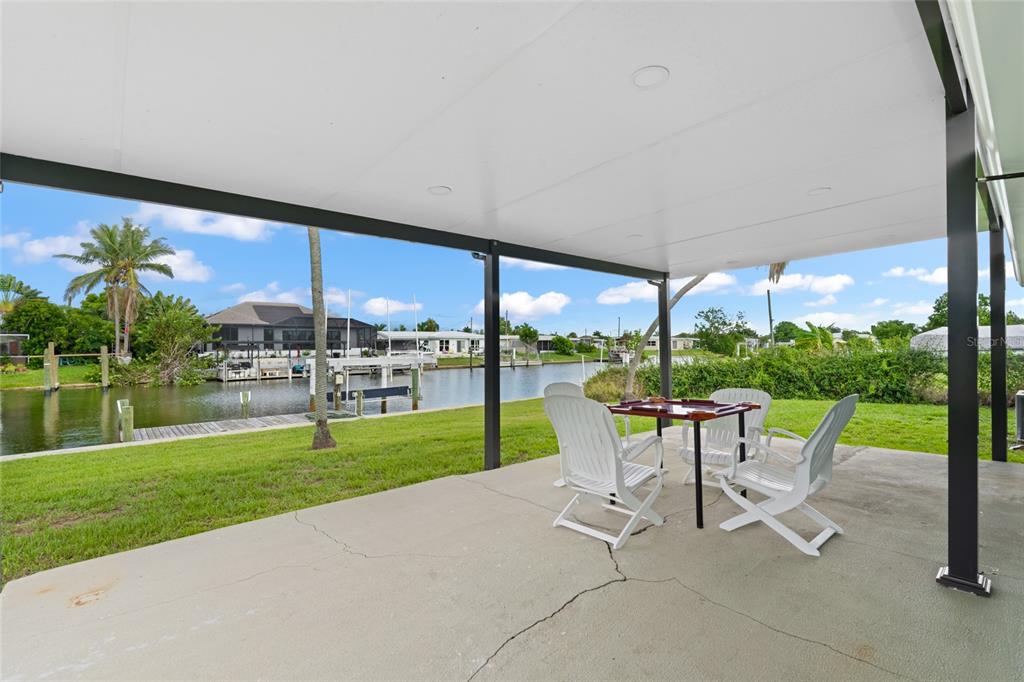A covered concrete patio overlooks a grassy lawn and a canal with boat docks — 21748 EDGEWATER DRIVE, PORT CHARLOTTE, FL