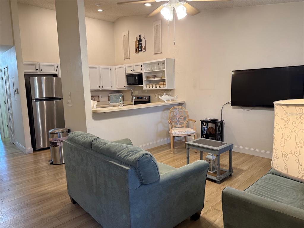A living room with light wood flooring opens to a kitchen featuring white cabinets — 1711 HAMMOCK PINE BOULEVARD UNIT 1711, CLEARWATER, FL