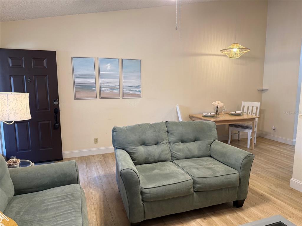 A living room with a green loveseat, a dining table, and a dark front door — 1711 HAMMOCK PINE BOULEVARD UNIT 1711, CLEARWATER, FL