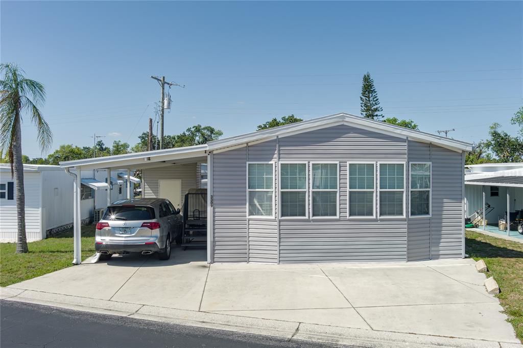 A gray manufactured home features a concrete driveway, a carport, and a row of windows — 3309 BERNADETTE DRIVE, ELLENTON, FL