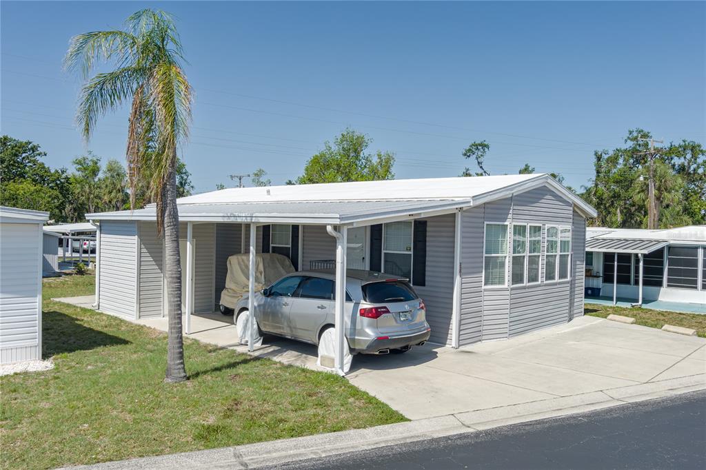 A gray manufactured home features a metal roof, a carport with a car, and palm trees — 3309 BERNADETTE DRIVE, ELLENTON, FL