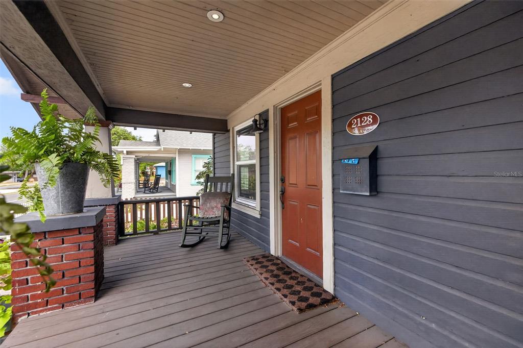 A covered front porch features a dark wood floor, a rocking chair, and a red door — 2128 5TH AVENUE N, ST PETERSBURG, FL