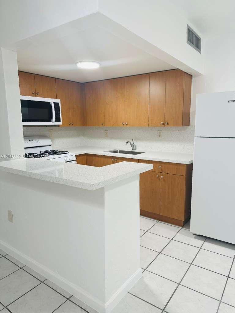 A kitchen features light-colored countertops, wooden cabinets, white appliances, and white tile flooring — 1230 W 54th St # 202A, Hialeah FL 33012, HIALEAH, FL