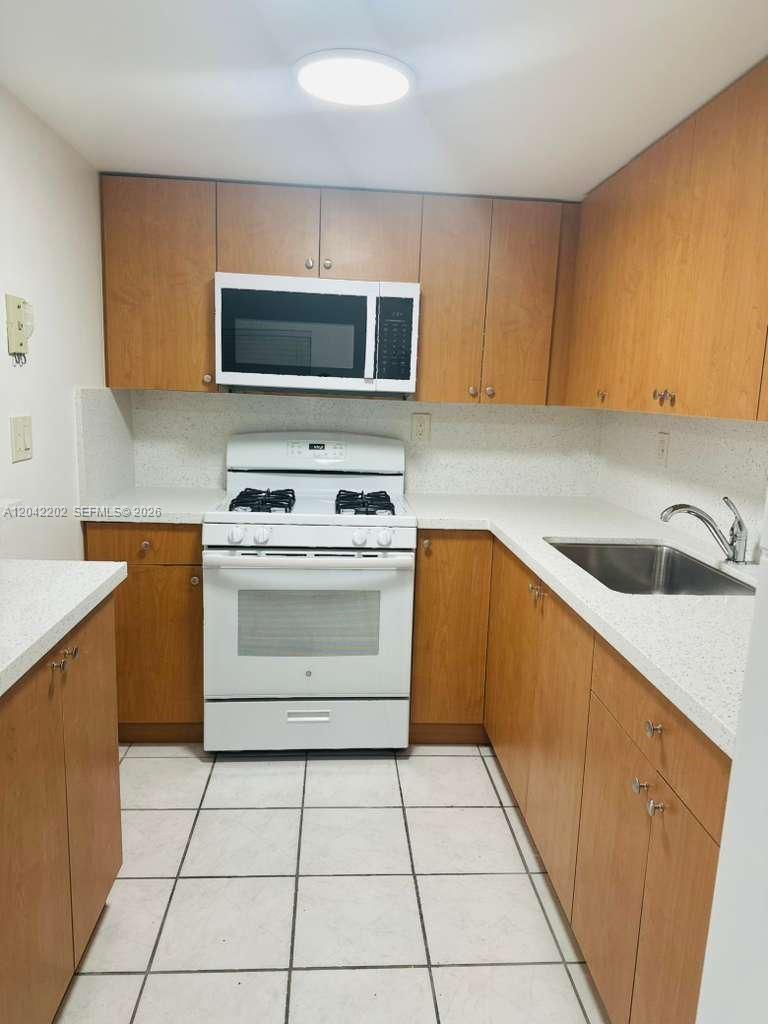 A kitchen features wood cabinets, white appliances, a white countertop, and light-colored floor tiles — 1230 W 54th St # 202A, Hialeah FL 33012, HIALEAH, FL