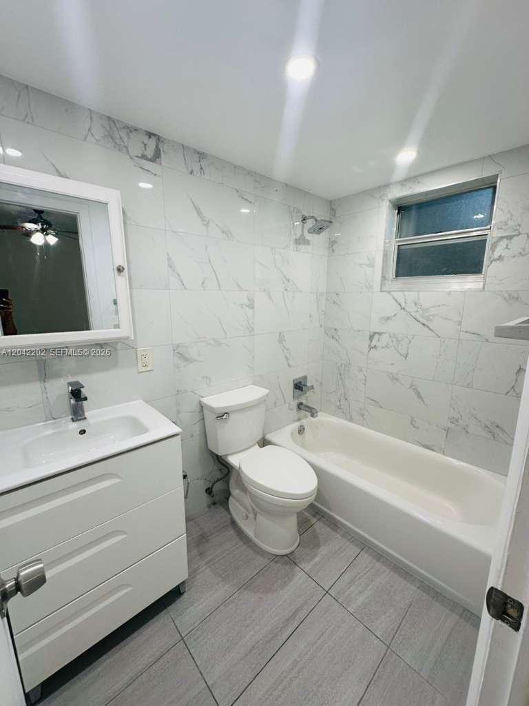 A bathroom features a white vanity, a toilet, and a bathtub with marble-style wall tiles — 1230 W 54th St # 202A, Hialeah FL 33012, HIALEAH, FL
