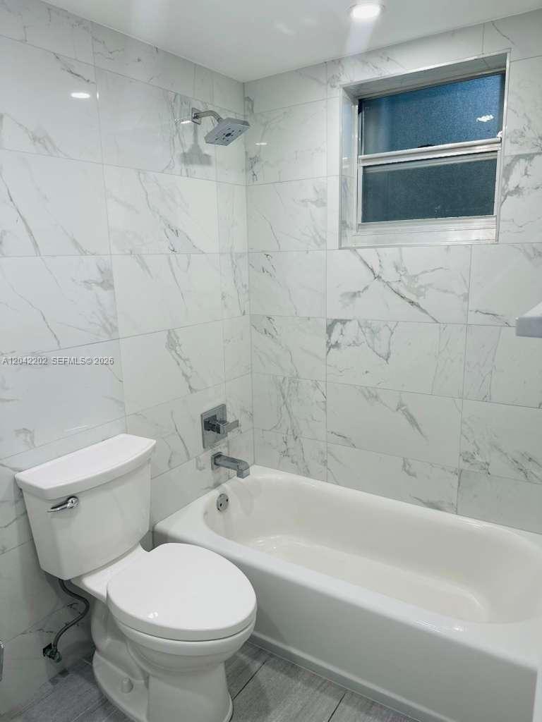 A bathroom features a white toilet, a bathtub, and white marble-patterned wall tiles — 1230 W 54th St # 202A, Hialeah FL 33012, HIALEAH, FL
