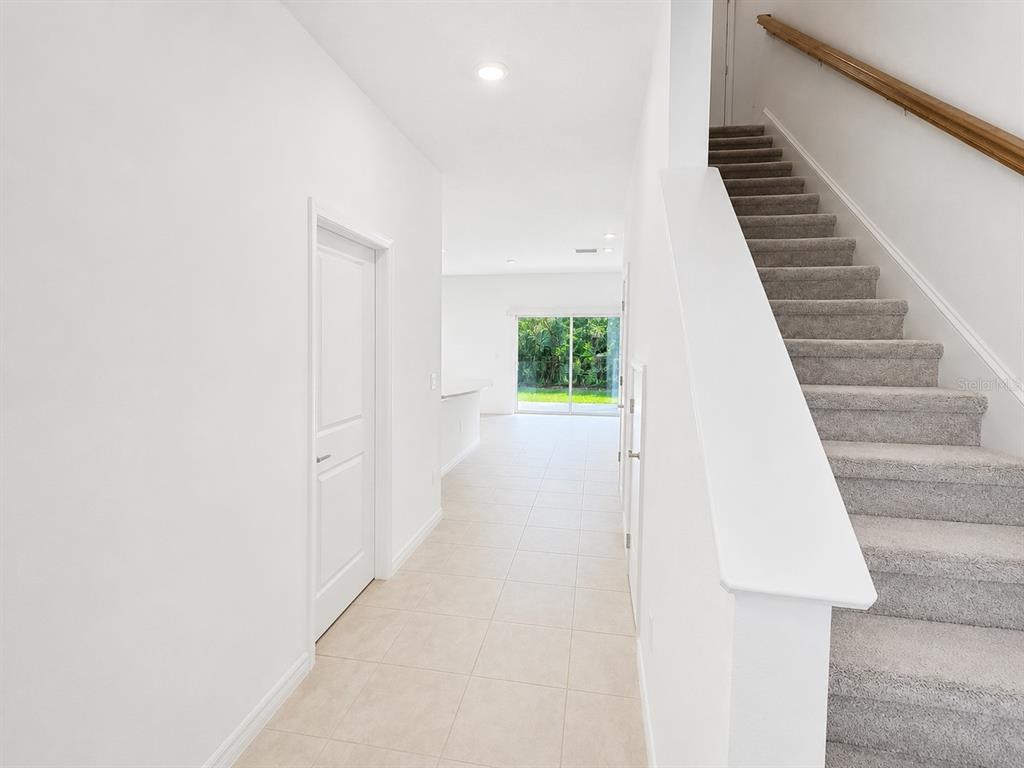 A hallway with tile flooring leads to a sliding glass door beside a carpeted staircase — 15144 CUZCORRO COURT, NOKOMIS, FL