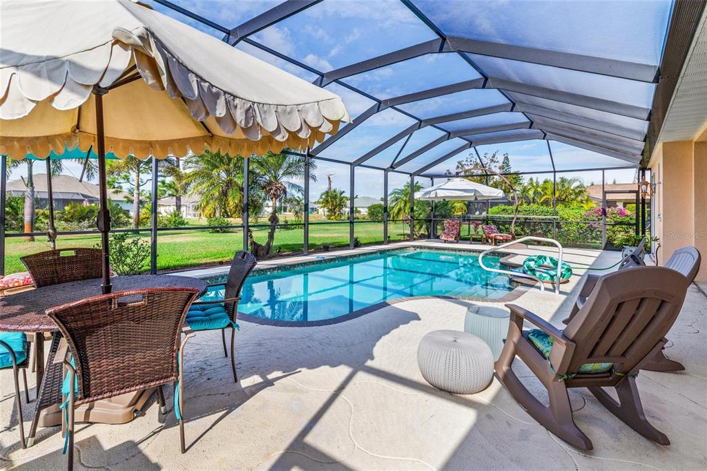 A screened-in pool patio features a dining set, lounge chairs, and a view of grass — 245 ROTONDA BOULEVARD N, ROTONDA WEST, FL