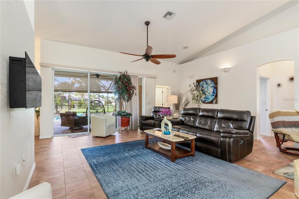 A living room with tile floors, a large blue rug, and sliding glass doors — 245 ROTONDA BOULEVARD N, ROTONDA WEST, FL