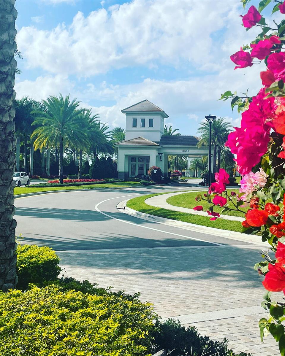 A gated community entrance with a guardhouse, palm trees, and bright pink bougainvillea in foreground — 7754 Monarch Court, Delray Beach FL 33446, DELRAY BEACH, FL