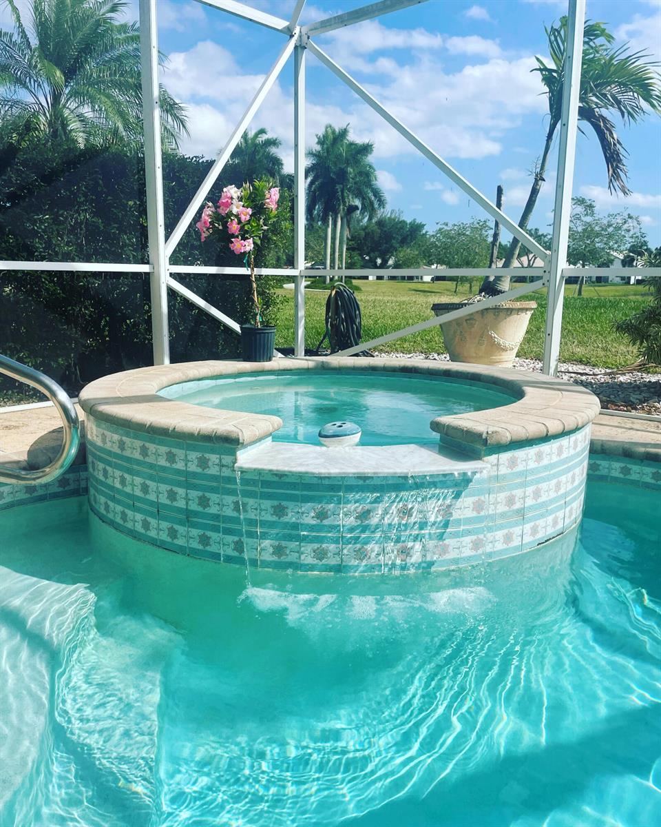 A round, tiled hot tub spills water into a swimming pool inside a screened enclosure — 7754 Monarch Court, Delray Beach FL 33446, DELRAY BEACH, FL