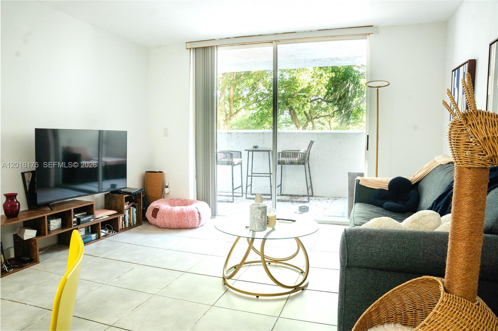 A living room features tile flooring, a television on a wooden stand, and a balcony — 750 NE 64th St # B215, Miami FL 33138, MIAMI, FL