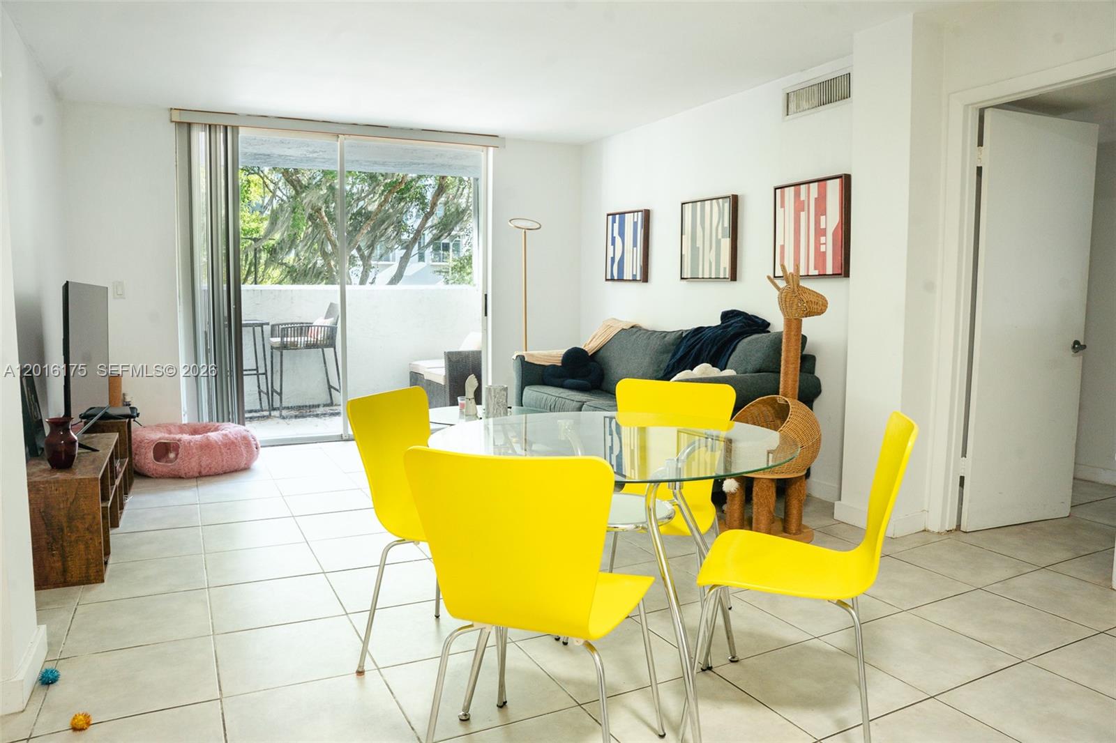 A living and dining area features yellow chairs, a glass table, and a sliding glass door — 750 NE 64th St # B215, Miami FL 33138, MIAMI, FL