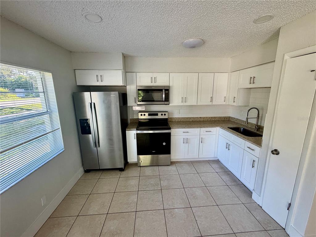 A kitchen features white cabinets, stainless steel appliances, granite countertops, and light-colored tile flooring — 10123 N 11TH STREET UNIT A, TAMPA, FL