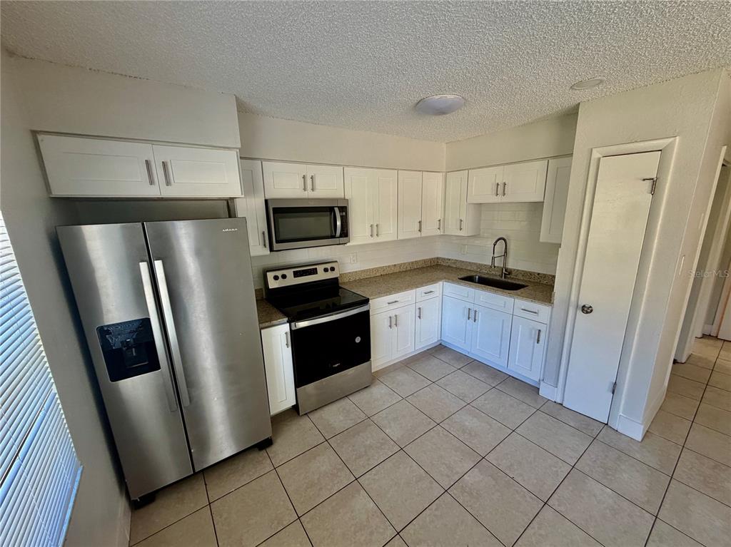 A kitchen features white cabinets, stainless steel appliances, granite countertops, and light-colored tile flooring — 10123 N 11TH STREET UNIT A, TAMPA, FL