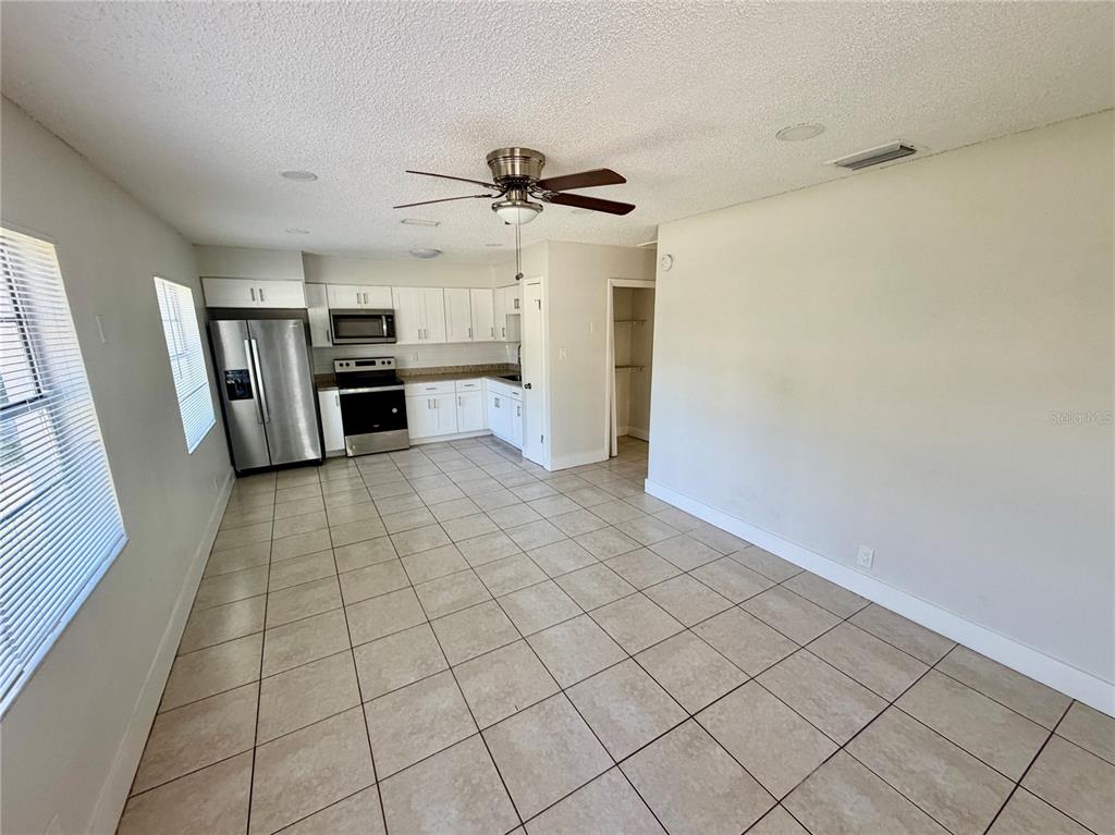 A kitchen with white cabinets, stainless steel appliances, and tile flooring opens to a room — 10123 N 11TH STREET UNIT A, TAMPA, FL