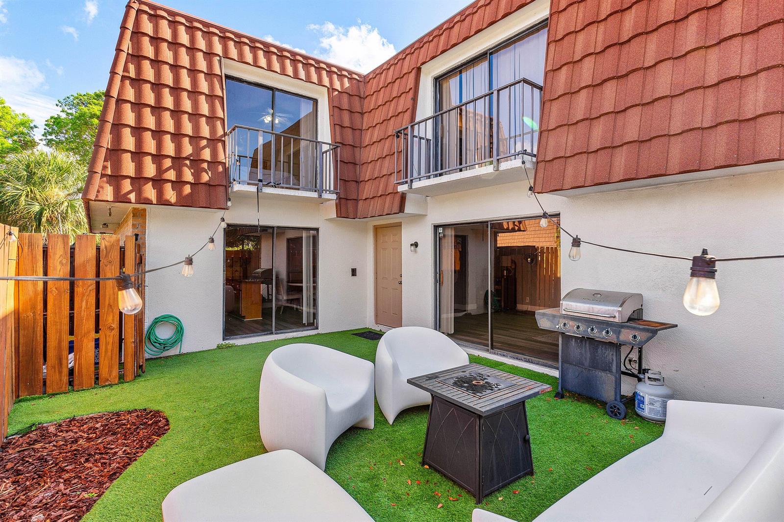 A backyard patio features artificial turf, white modern furniture, a fire pit, and a grill — 3425 San Bernadino Drive # b, Delray Beach FL 33445, DELRAY BEACH, FL