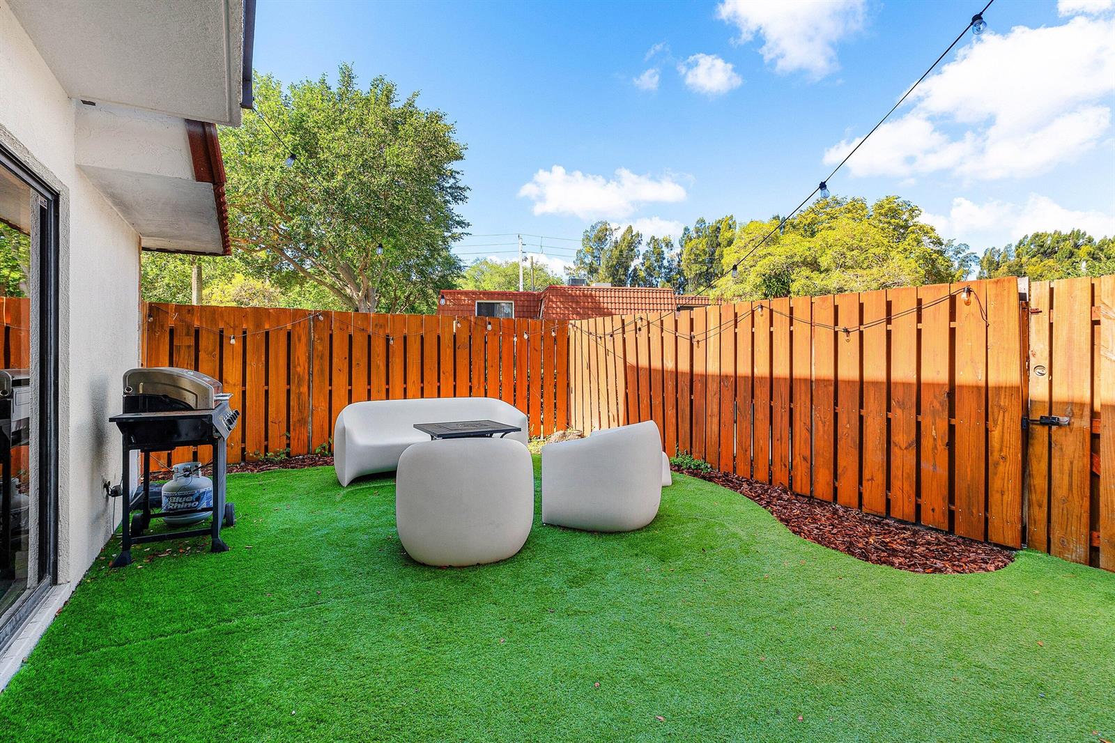 A small backyard features artificial turf, a wooden privacy fence, and modern white patio furniture — 3425 San Bernadino Drive # b, Delray Beach FL 33445, DELRAY BEACH, FL