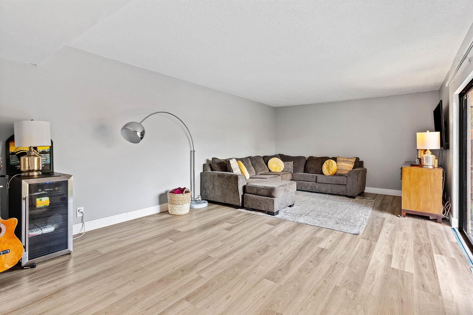 A living room features gray walls, wood-look flooring, a sectional sofa, and a floor lamp — 3425 San Bernadino Drive # b, Delray Beach FL 33445, DELRAY BEACH, FL