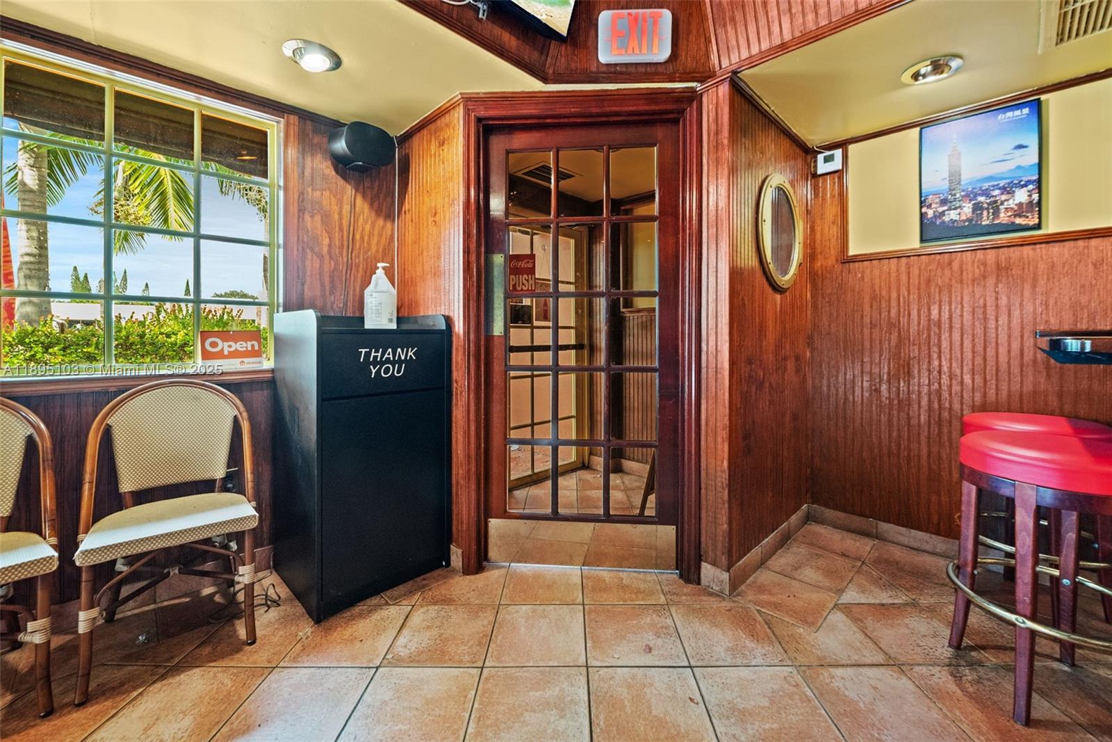 A wood-paneled room features a glass-paned door, a black trash receptacle, and red bar stools — 6330 Miramar Pkwy, Miramar FL 33023, MIRAMAR, FL