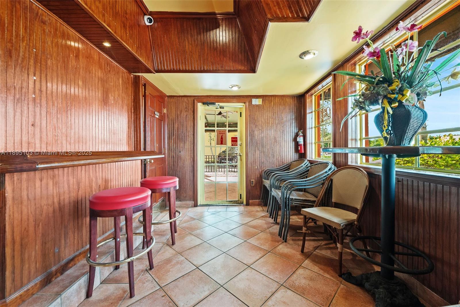 A room with wood-paneled walls, tile flooring, a bar with stools, and outdoor views — 6330 Miramar Pkwy, Miramar FL 33023, MIRAMAR, FL