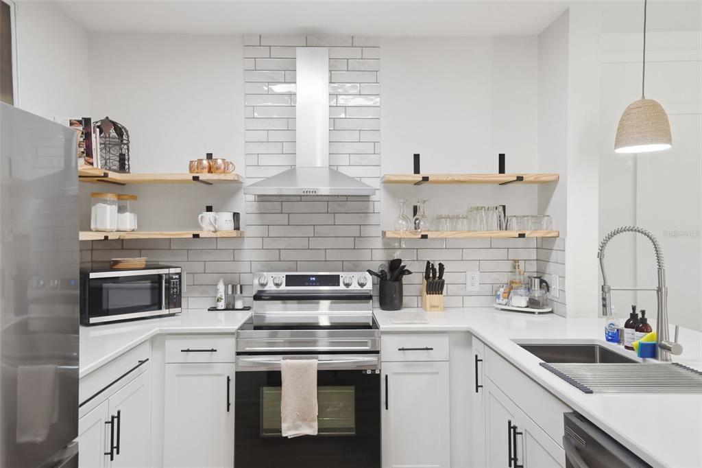 A modern kitchen features white cabinets, stainless steel appliances, open wood shelving, and subway tile — 3176 FELTRIM PLACE UNIT 302, KISSIMMEE, FL