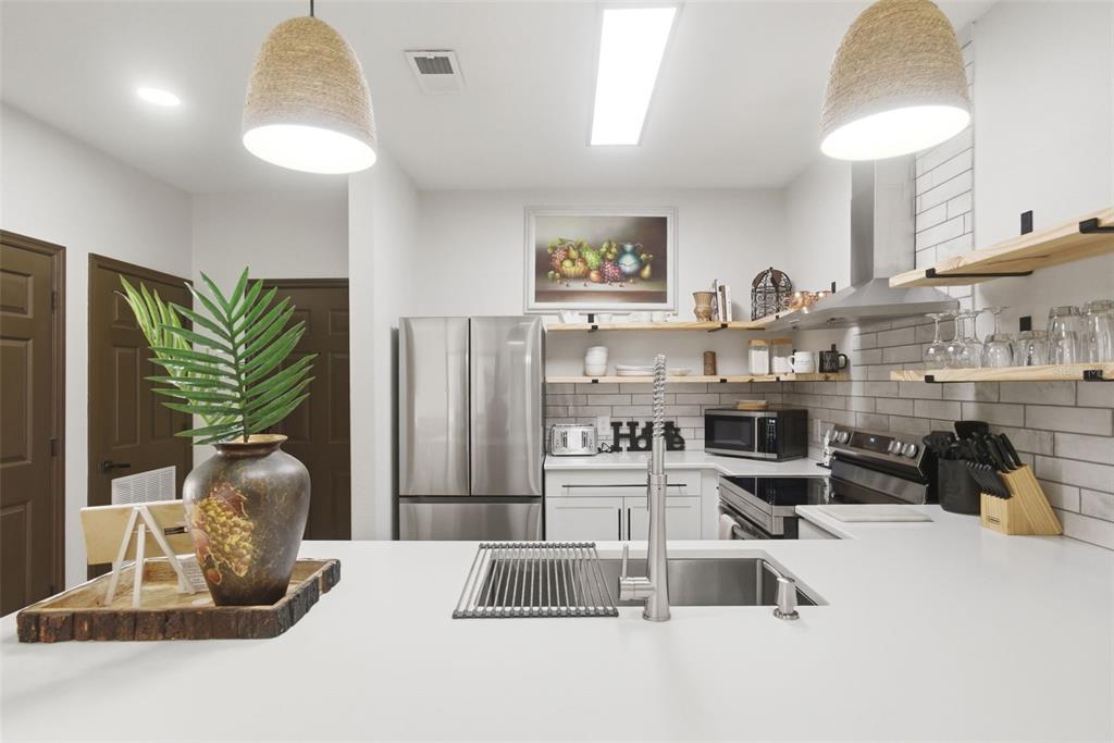 A kitchen features white countertops, stainless steel appliances, open wood shelving, and two pendant lights — 3176 FELTRIM PLACE UNIT 302, KISSIMMEE, FL