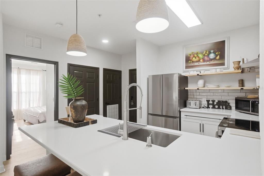 A modern kitchen features a white quartz island, stainless steel appliances, and open wood shelving — 3176 FELTRIM PLACE UNIT 302, KISSIMMEE, FL