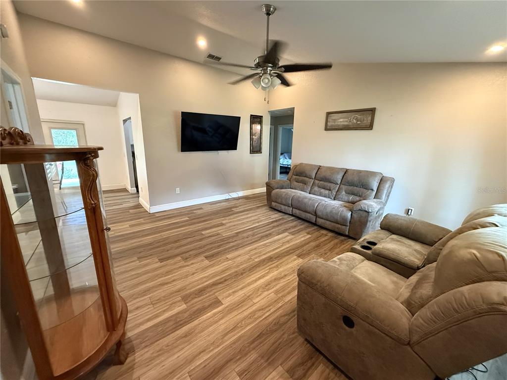 A living room features wood-look flooring, a ceiling fan, a wall-mounted television, and reclining furniture — 10 EMERALD TRAIL, OCALA, FL