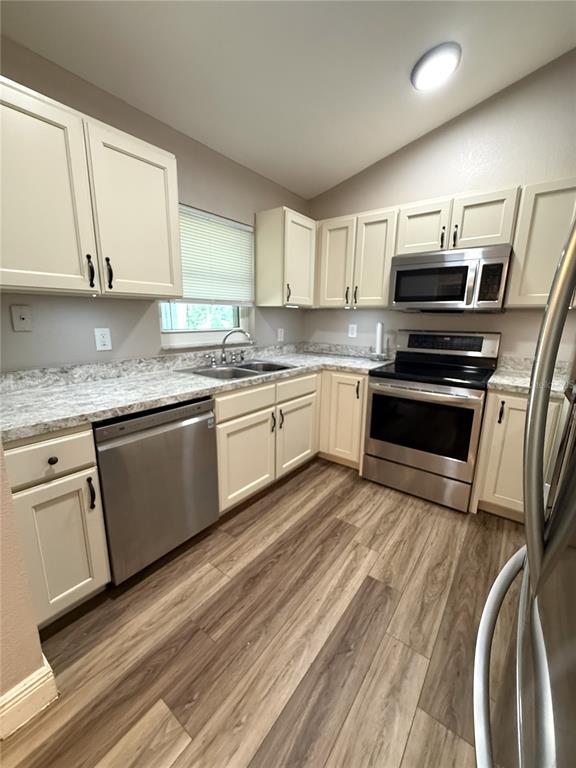 A kitchen features cream-colored cabinets, stainless steel appliances, and wood-look flooring — 10 EMERALD TRAIL, OCALA, FL