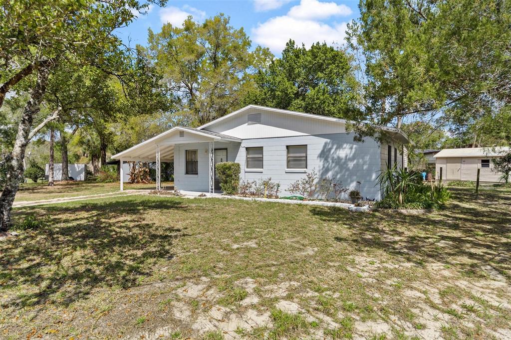 A light-colored, single-story house with a carport sits on a grassy, partially shaded lot — 501 POINSETTIA AVENUE, FRUITLAND PARK, FL