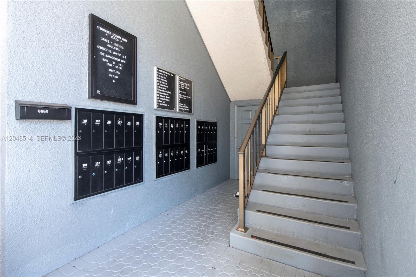 An indoor stairwell features gray walls, a metal railing, and rows of black mailboxes — 3801 N University Dr # 313, Sunrise FL 33351, SUNRISE, FL