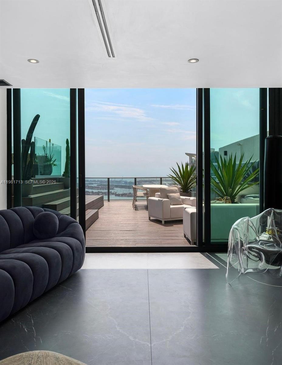 A modern living room opens through glass sliding doors to a wooden balcony overlooking water — 650 NE 32nd St, Miami FL 33137, MIAMI, FL