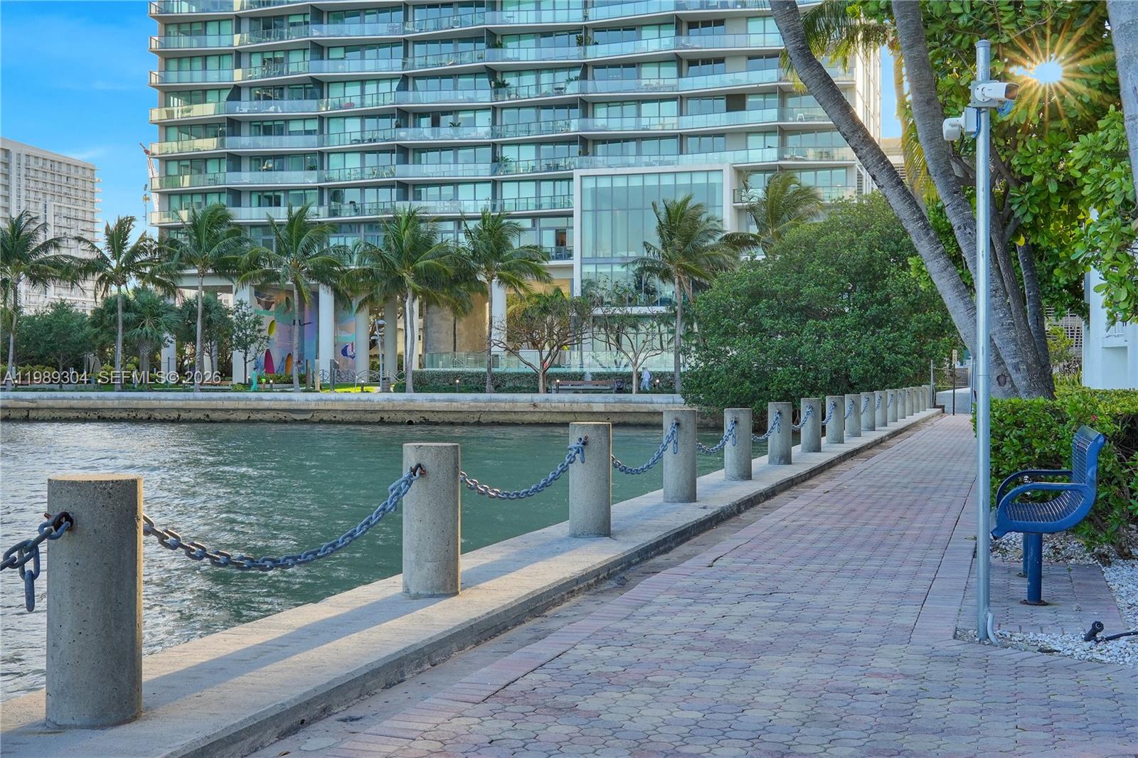 A paved waterfront walkway features concrete bollards with chain railings and a blue metal bench — 500 NE 29th St # 608, Miami FL 33137, MIAMI, FL
