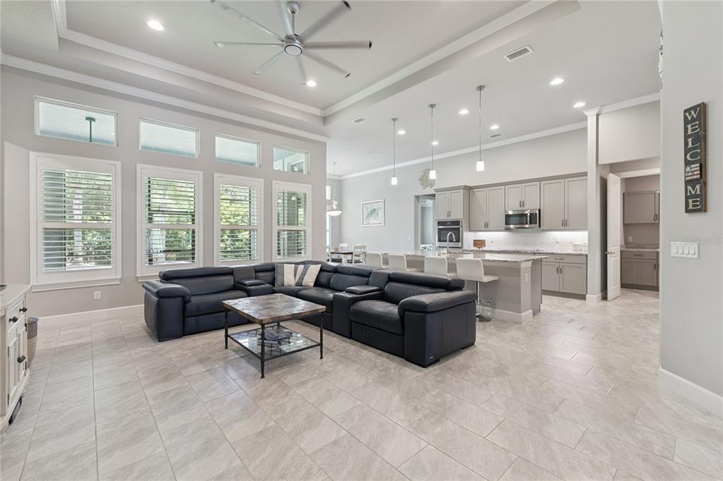 An open-concept living room and kitchen featuring gray cabinetry, tile flooring, and a large sectional — 2423 WILD TURKEY CREEK LANE, PORT ORANGE, FL