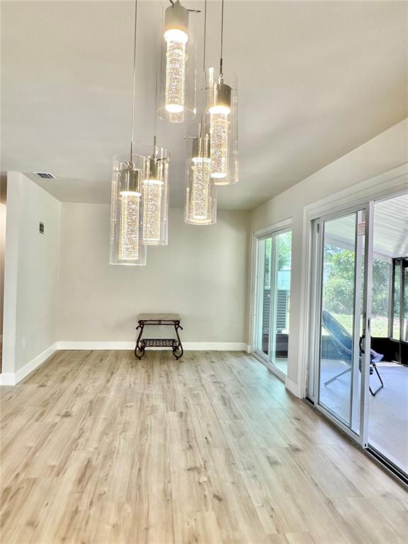 A dining area features light wood-look flooring, a modern multi-pendant light fixture, and sliding glass doors — 400 DALTON BOULEVARD, PORT CHARLOTTE, FL