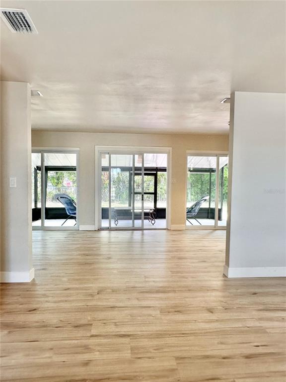 A living area with light wood-look flooring features three sliding glass doors leading to a lanai — 400 DALTON BOULEVARD, PORT CHARLOTTE, FL