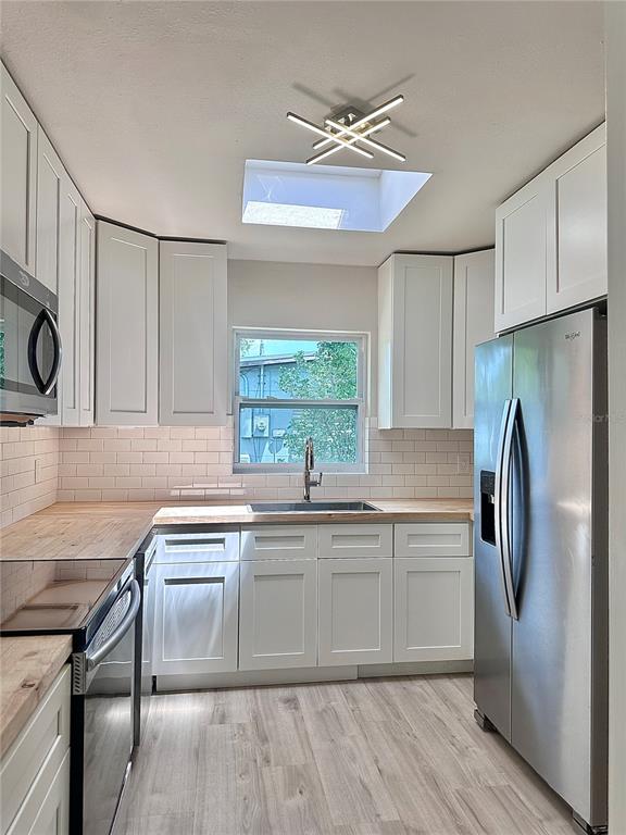 A kitchen features white cabinets, light wood countertops, stainless steel appliances, and a skylight — 400 DALTON BOULEVARD, PORT CHARLOTTE, FL