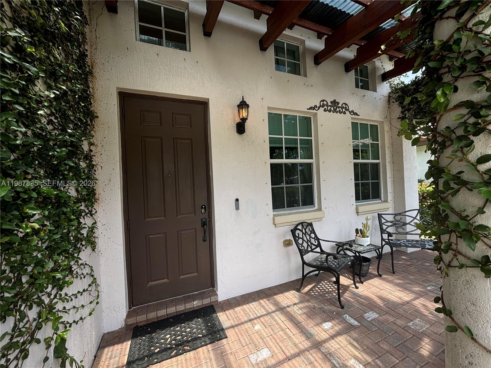A white stucco exterior features a brown door, two windows, and a brick patio — 8080 NW 126th Ter, Parkland FL 33076, PARKLAND, FL