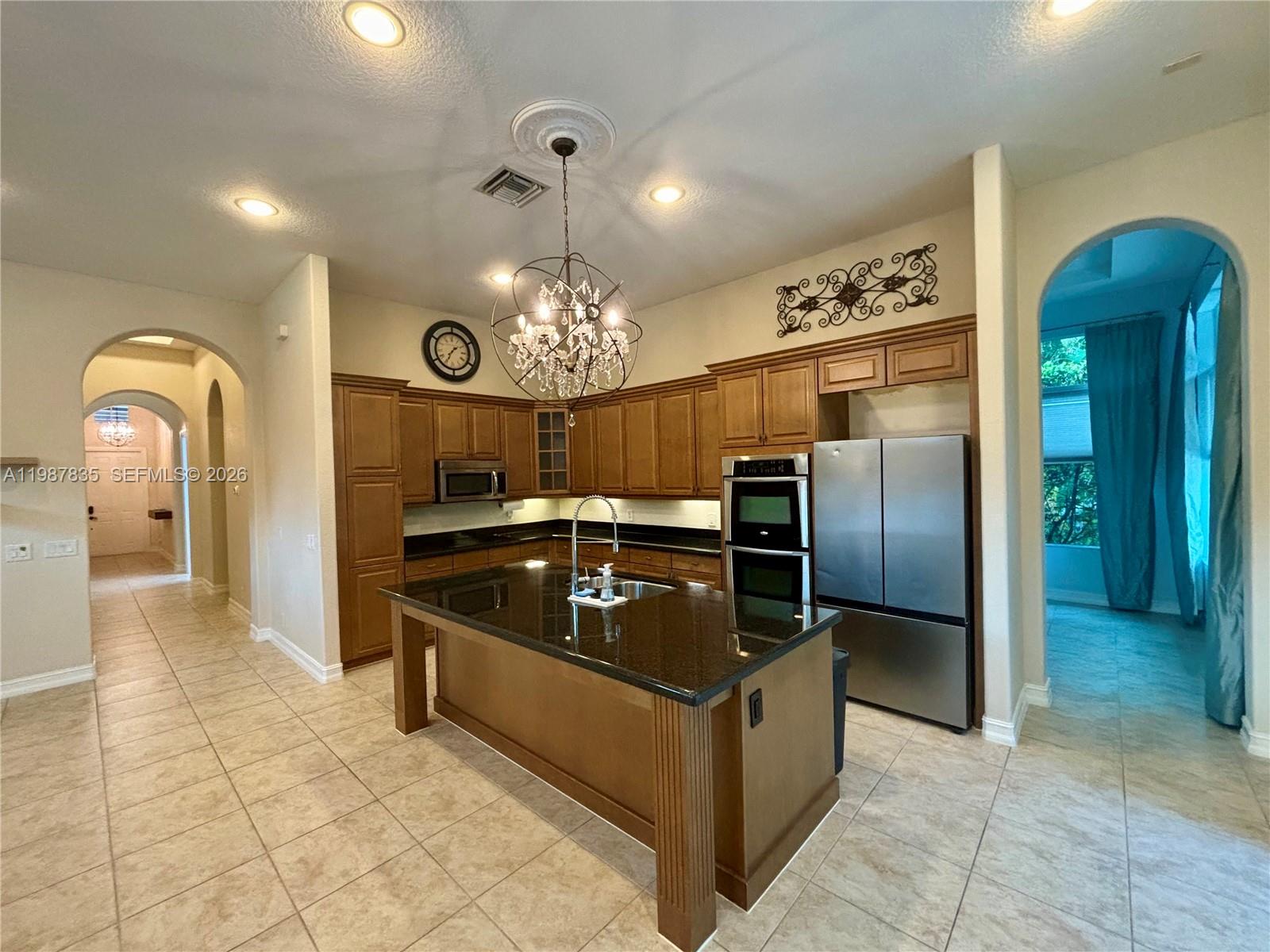 A kitchen features wood cabinets, a black granite island, stainless steel appliances, and tile flooring — 8080 NW 126th Ter, Parkland FL 33076, PARKLAND, FL