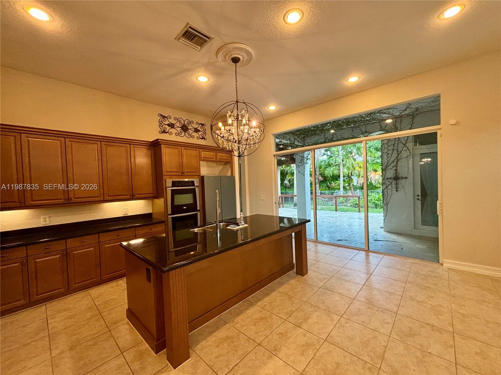 A kitchen features dark wood cabinets, black countertops, a central island, and sliding glass doors — 8080 NW 126th Ter, Parkland FL 33076, PARKLAND, FL