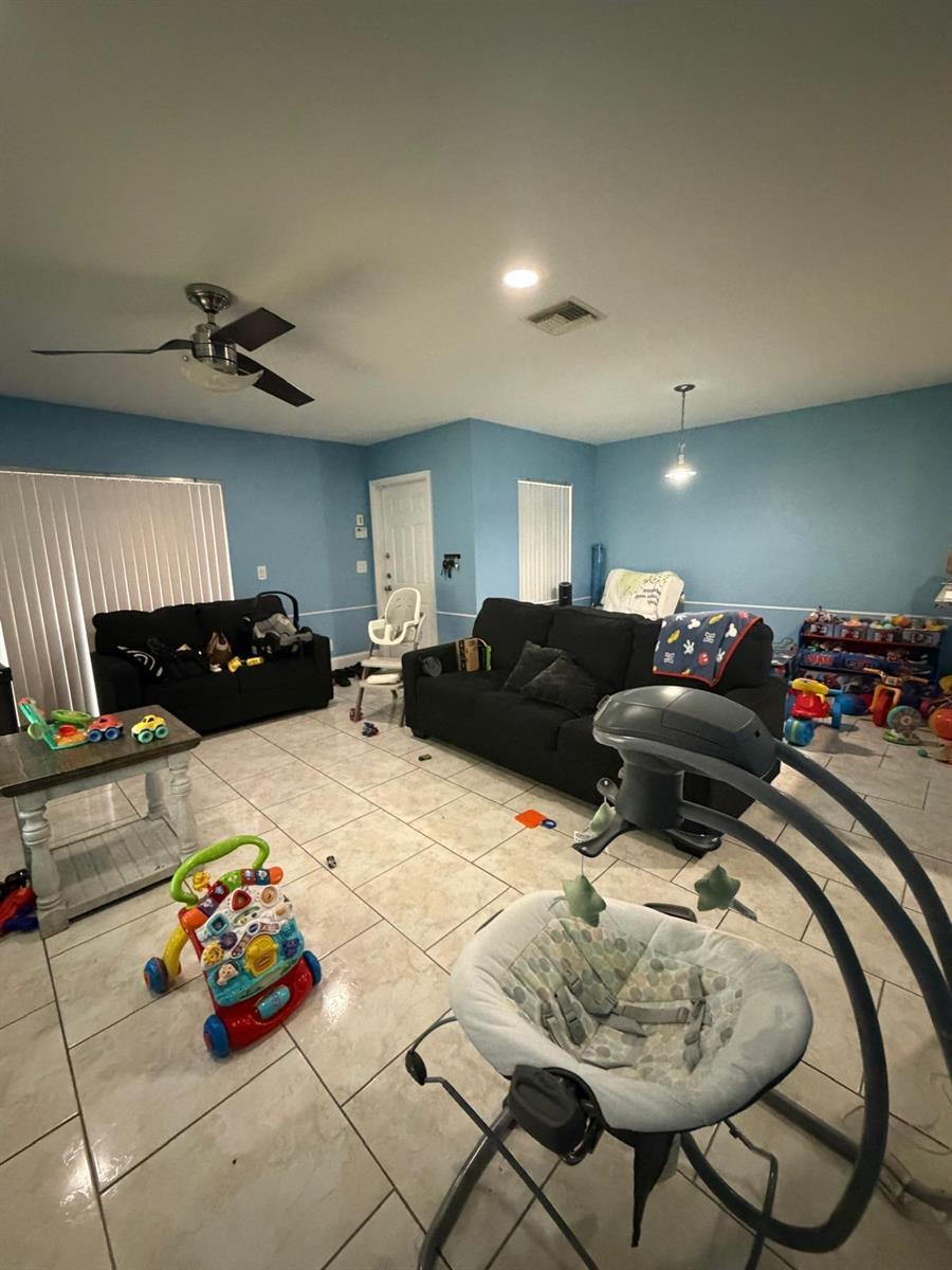 A living room with blue walls, tile flooring, two black sofas, and various baby items — 5362 SW 125th Avenue, Miramar FL 33027, MIRAMAR, FL