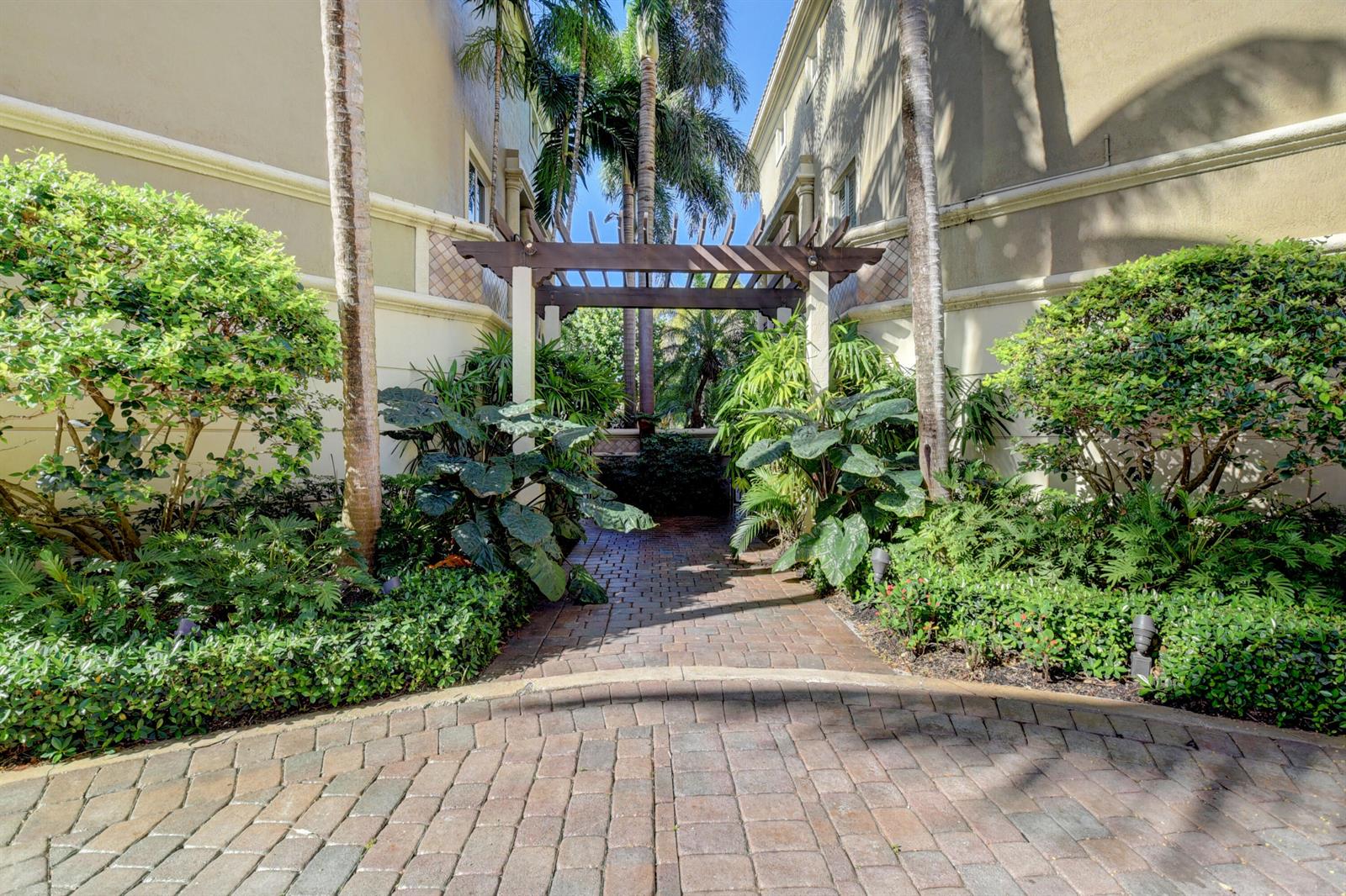 A brick walkway leads through a wooden pergola between two buildings surrounded by lush landscaping — 921 Osceola Drive Unit 4, Boca Raton FL 33432, BOCA RATON, FL