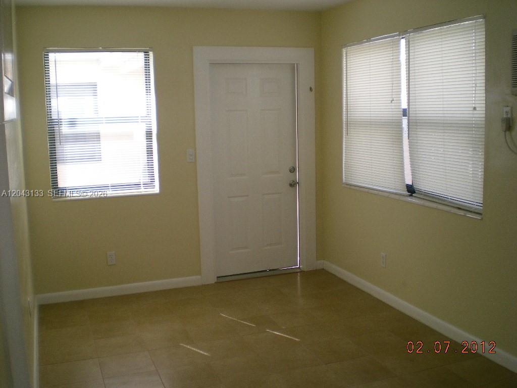 A room with light yellow walls, tile flooring, two windows with blinds, and a door — HOLLYWOOD, FL