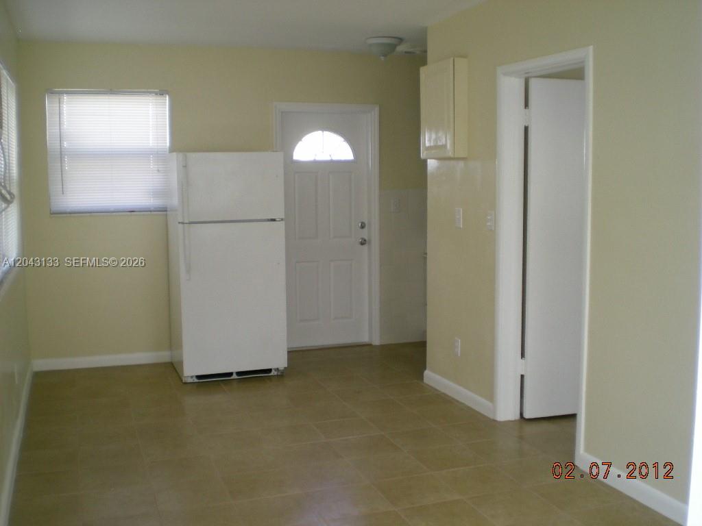 A kitchen features a white refrigerator, tiled floors, a window with blinds, and a doorway — HOLLYWOOD, FL