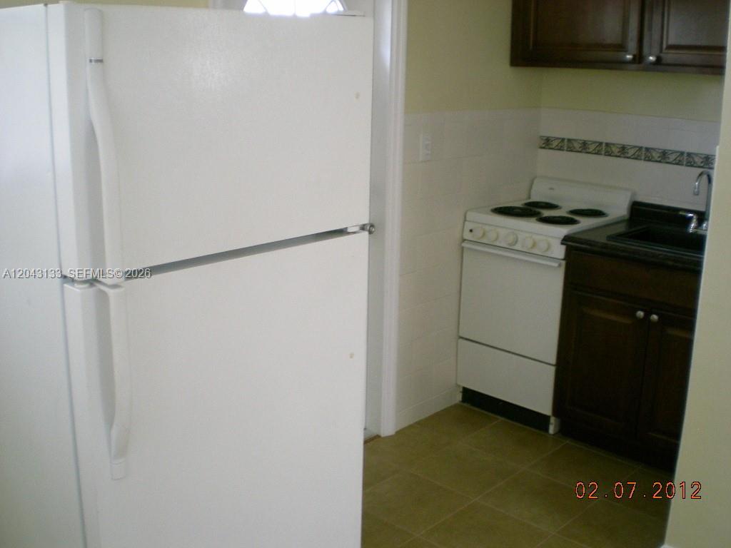 A white refrigerator stands next to a small kitchen with a stove and sink — HOLLYWOOD, FL