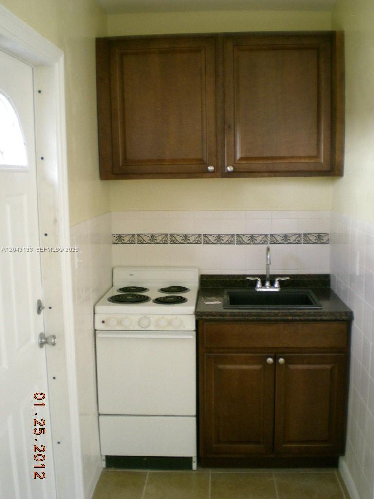 A small kitchenette features a white stove, a dark sink, and brown wooden cabinets — HOLLYWOOD, FL